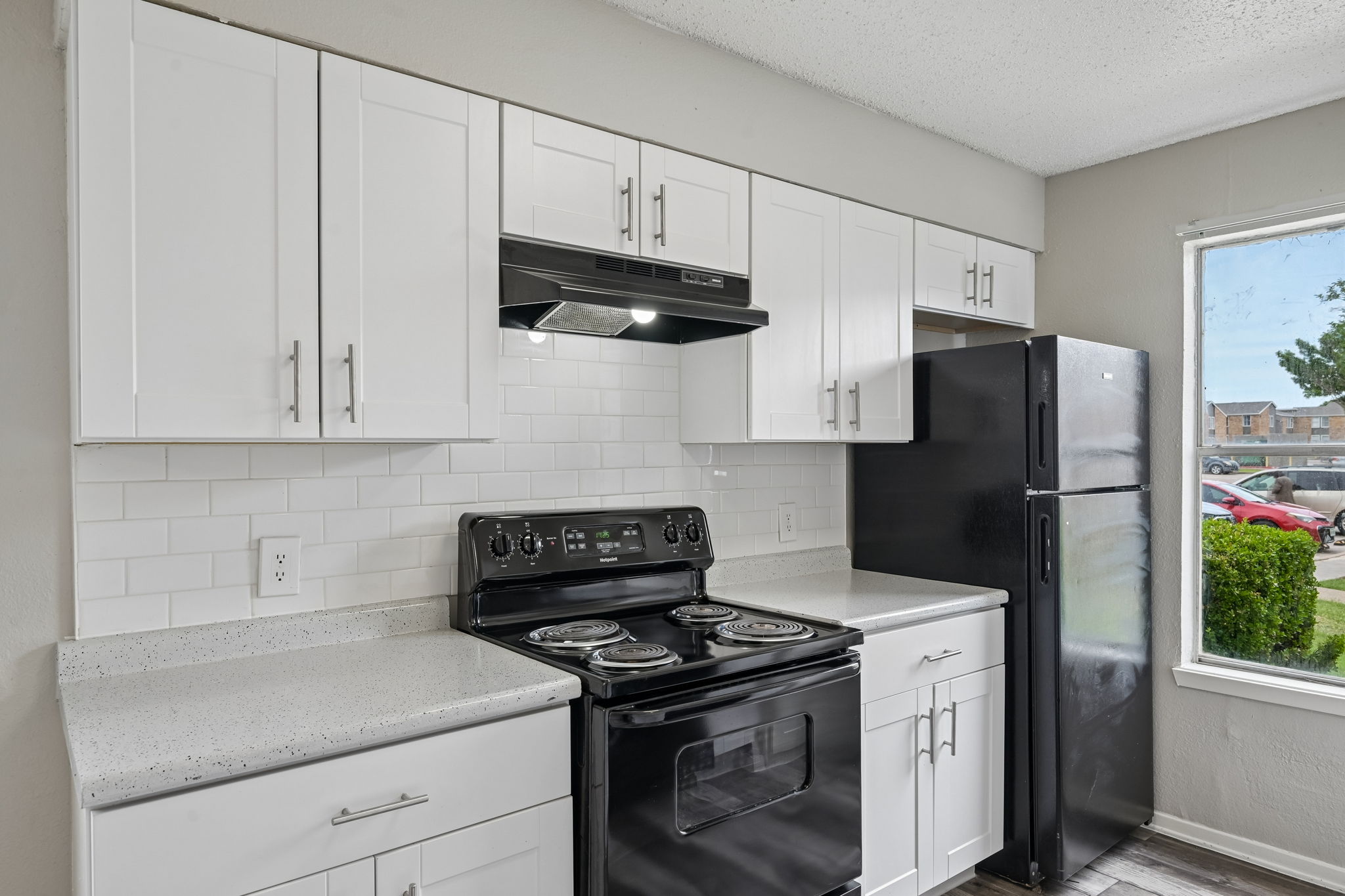 A black refrigerator stands next to a stove in a kitchen with white cabinets.